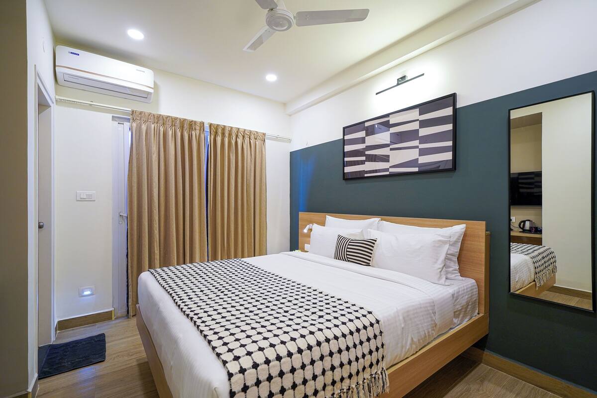 A bedroom with a bed, a ceiling fan, an air conditioning unit, a door, and a curtain.