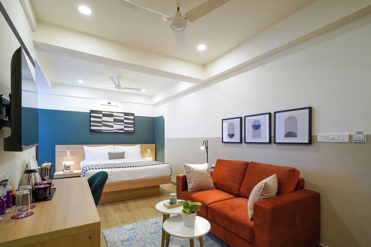 A modern hotel room with a bed, a sofa, a desk, and a TV.