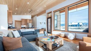 Een moderne woonkamer met een bank, salontafel en grote ramen met uitzicht op een besneeuwd landschap.