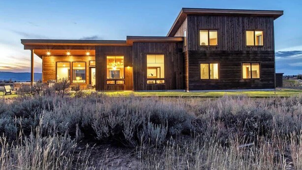 Een modern huis met twee verdiepingen, met een houten gevel, grote ramen en een verlichte veranda.