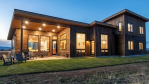 Een modern huis met twee verdiepingen, een ruime overdekte patio, meerdere ramen en een verzorgd gazon.
