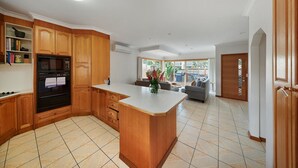 A modern kitchen with wooden cabinets, a built-in oven, and a large island. - Sandy Bliss - Walk to the beach (Torquay)