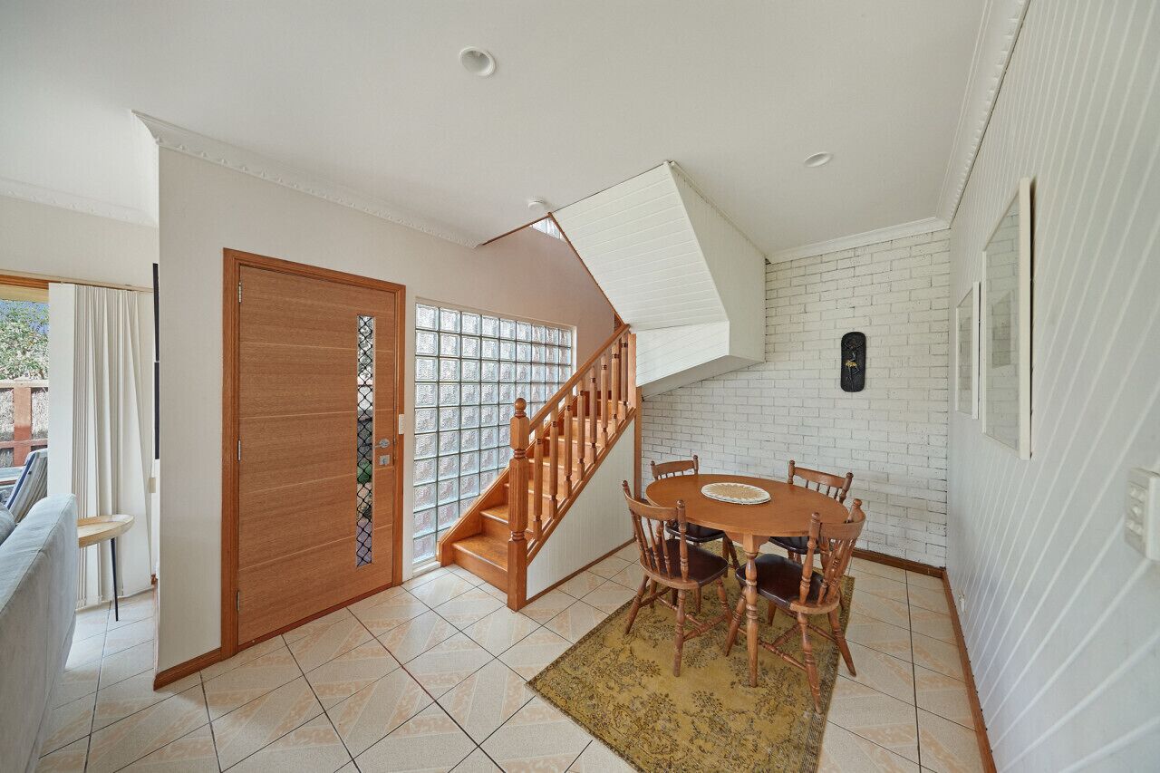Un coin repas avec une table et des chaises en bois, un escalier avec des rampes en bois et un mur en briques blanches.