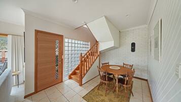 Un coin repas avec une table et des chaises en bois, un escalier avec des rampes en bois et un mur en briques blanches.