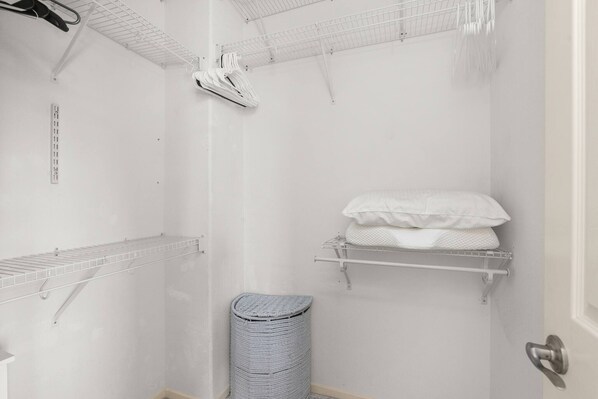 A white bathroom with a shower, a towel rack, a laundry basket, and a door.