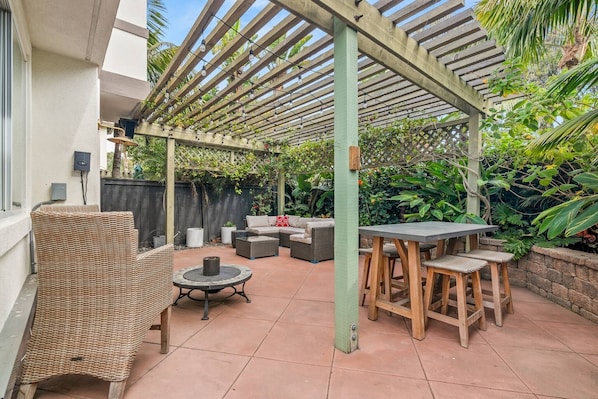Eine Terrasse im Freien mit Korbmöbeln, einem runden Tisch und einer Holzw pergola.