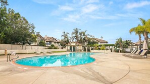 A swimming pool with a curved edge, surrounded by lounge chairs and palm trees.