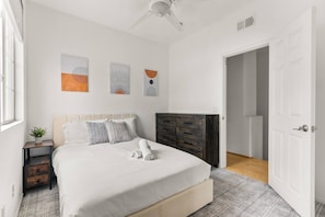 A bedroom with a bed, a dresser, a ceiling fan, and abstract wall art.