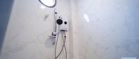 Un baño con azulejos de mármol blanco, ducha integrada con cabezal de ducha manual y una pequeña ventana circular.