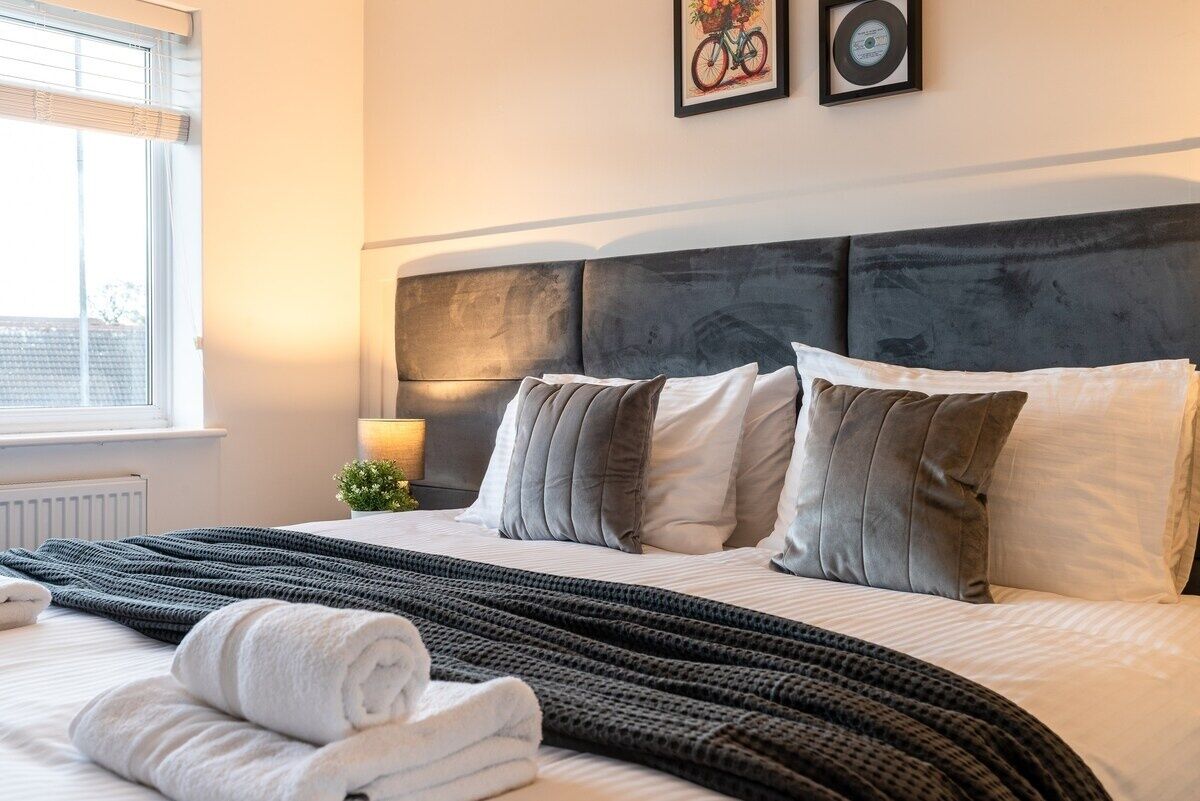 A neatly made bed with a grey headboard, white and grey pillows, and a dark grey knitted blanket.
