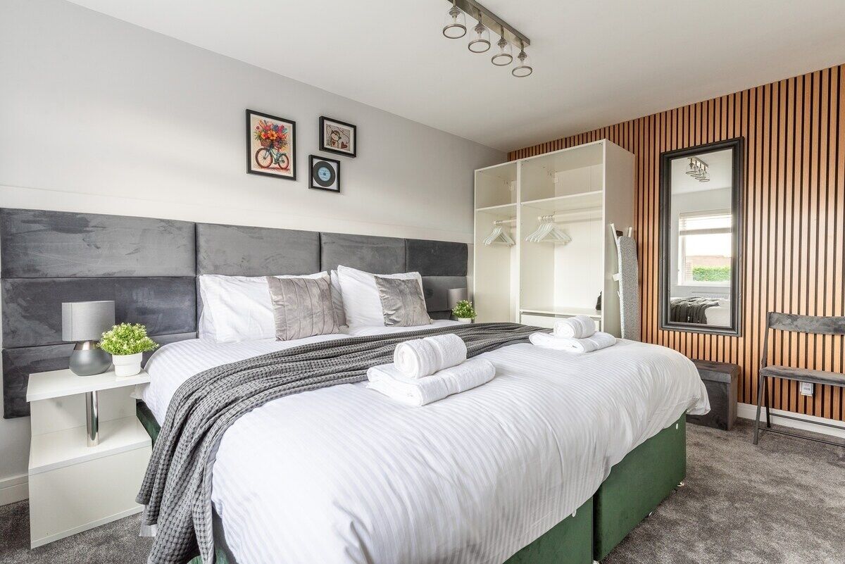 Een moderne slaapkamer met een groot bed, een garderobe, een spiegel en een nachtkastje.