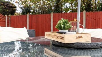 Une table ronde en verre, sur laquelle repose un plateau en bois, lui-même orné d’une petite plante en pot et d’un récipient en verre.