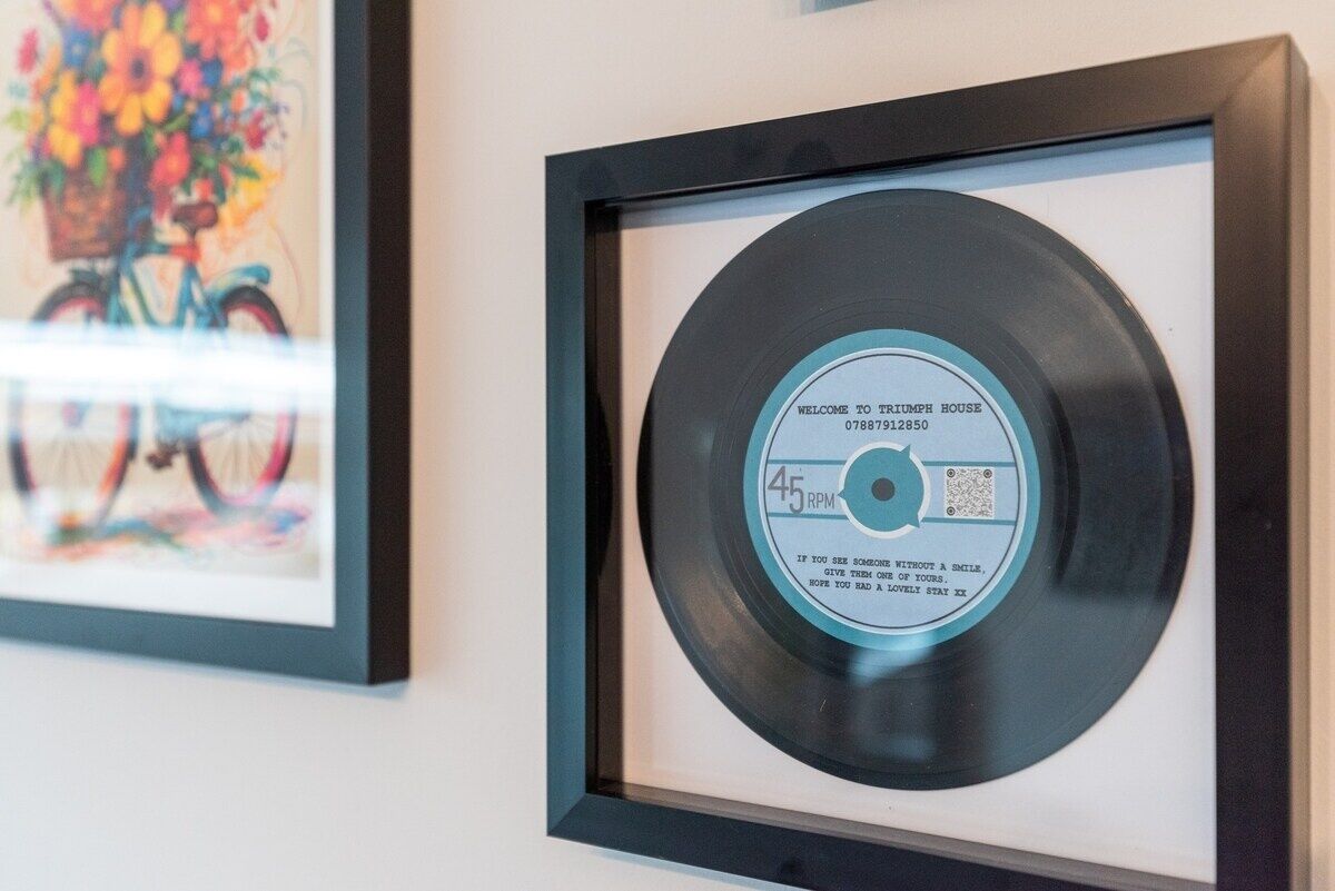 A framed vinyl record with a label that reads "WELCOME TO TRIUMPH HOUSE 07887912850 45 RPM".