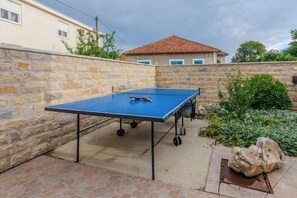 A ping pong table in an outdoor patio area with stone walls and a tiled floor.