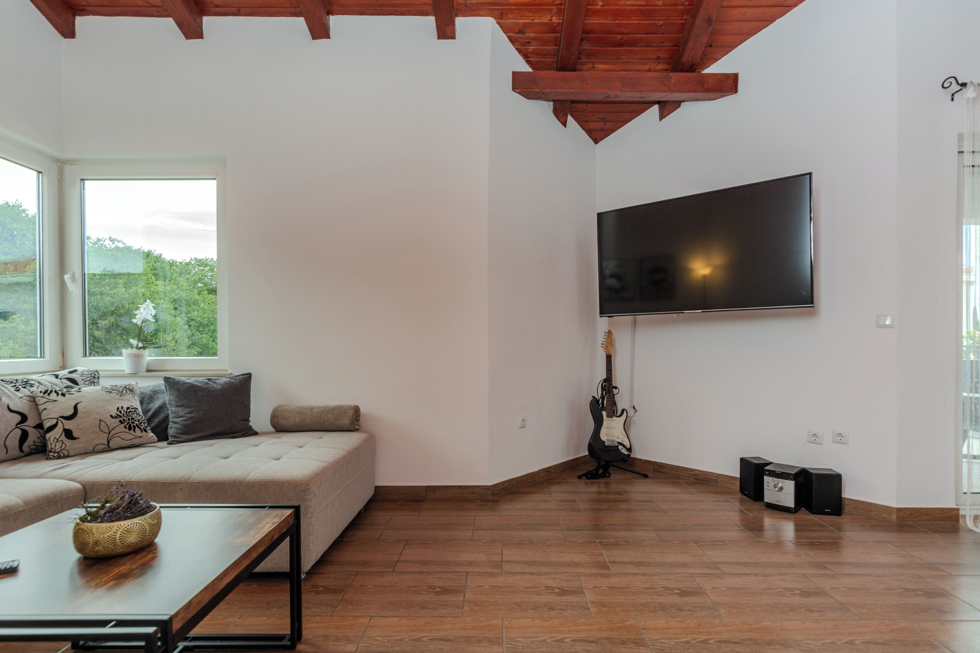 Una sala moderna con un ventanal grande, un sofá, una mesa de centro, una guitarra y un televisor de pantalla plana montado en la pared.