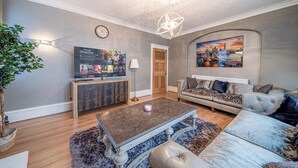 Ein Wohnzimmer mit einer Couch, einem Couchtisch, einer Lampe, einem Fernseher und einem Bild an der Wand.