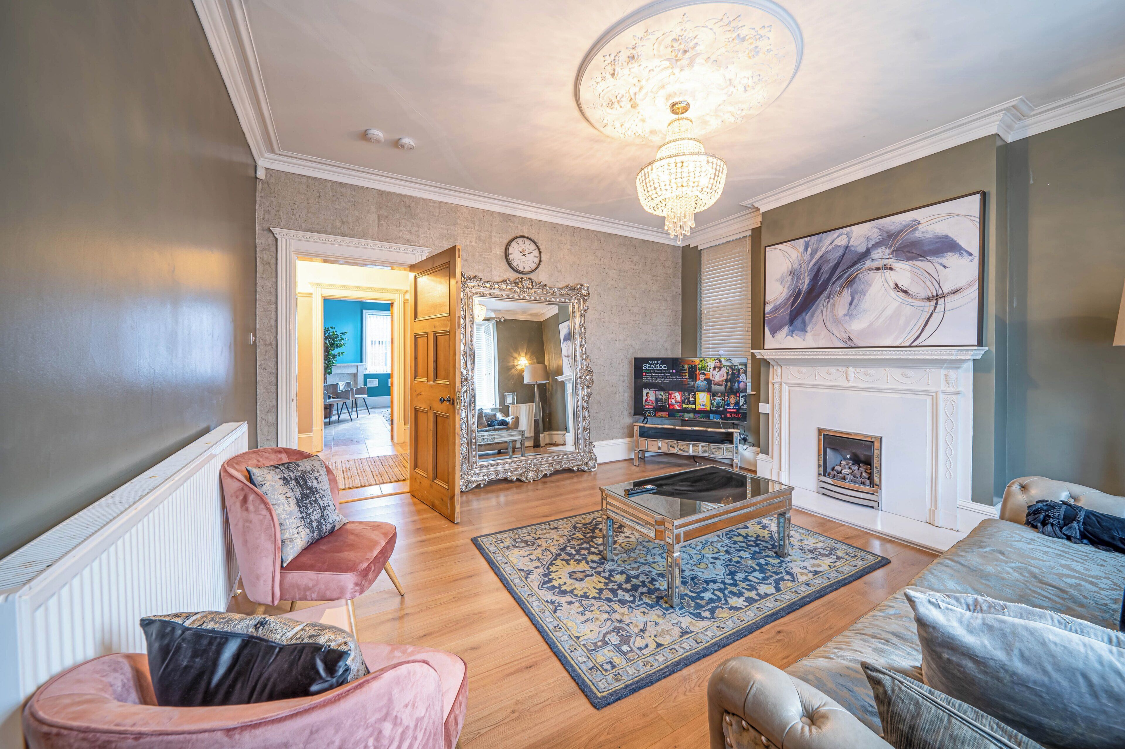 A spacious living room with a chandelier, a fireplace, and a large abstract painting.