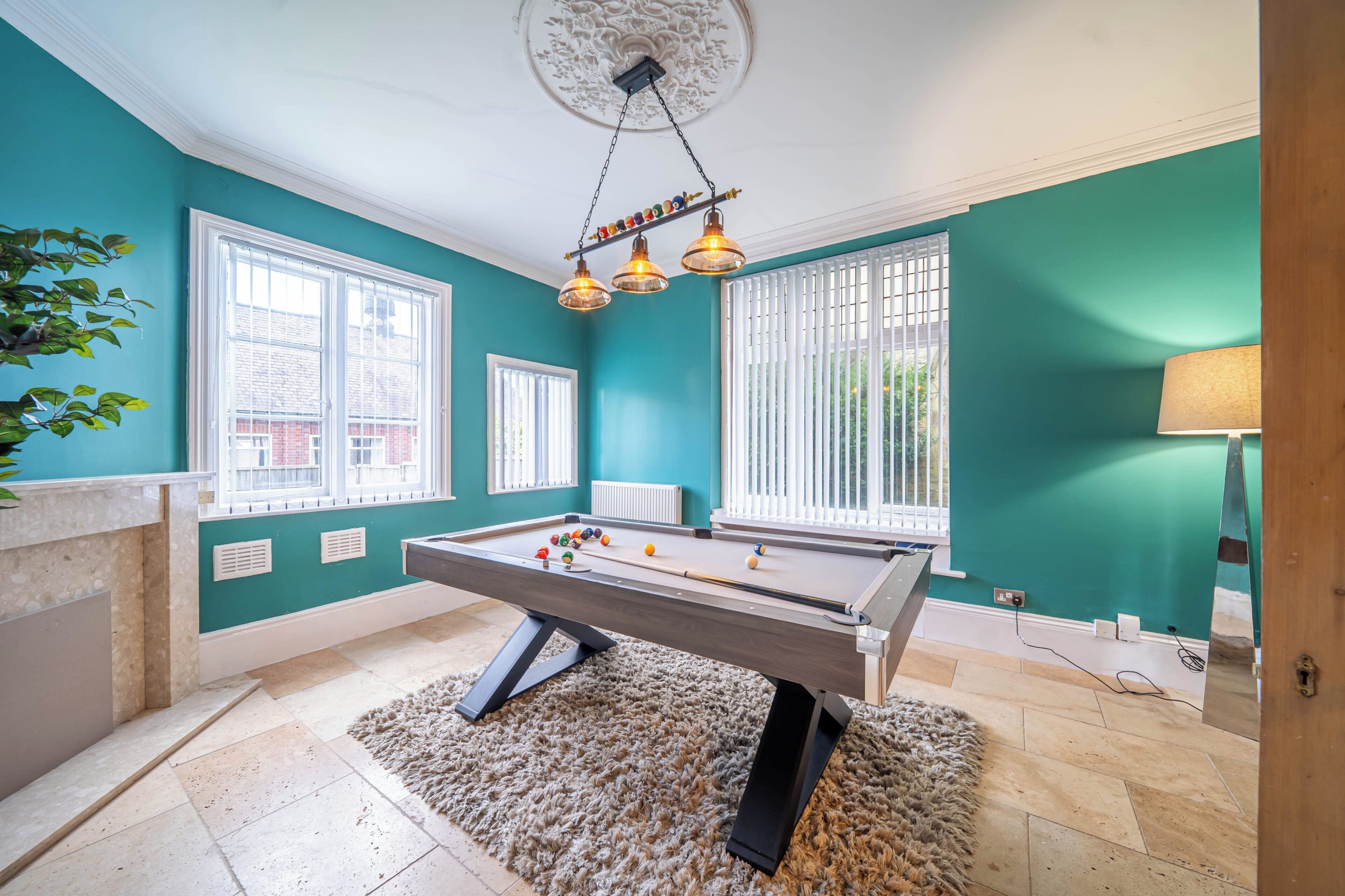 A pool table in a room with teal walls, large windows, and a ceiling light fixture.