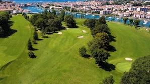 Vista aérea de un campo de golf con un puerto deportivo y edificios residenciales al fondo.