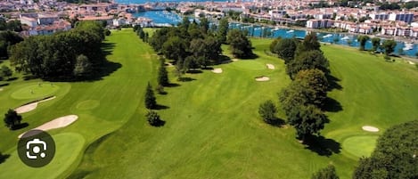 An aerial view of a golf course with a marina and residential buildings in the background.