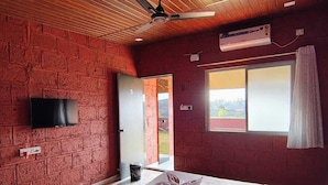 Une chambre avec un plafond en bois, un lit recouvert de draps blancs, un téléviseur à écran plat fixé au mur et une fenêtre donnant sur l’extérieur.