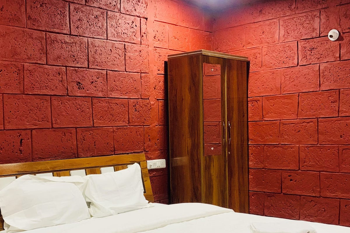 A bedroom with a wooden bed, a wardrobe, and a red brick wall.