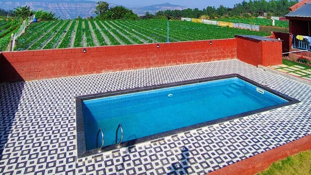Une piscine dotée d’une terrasse carrelée, entourée d’un mur rouge et bordée d’un sol à motifs.