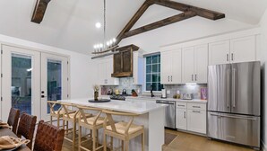 Cozinha moderna com armários brancos, uma grande geladeira de aço inoxidável e banquetas de madeira.