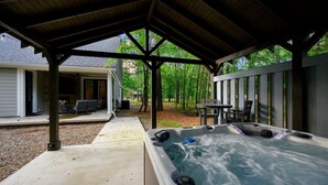 Área externa coberta com hidromassagem, um terraço, assentos e vista para uma casa e árvores.