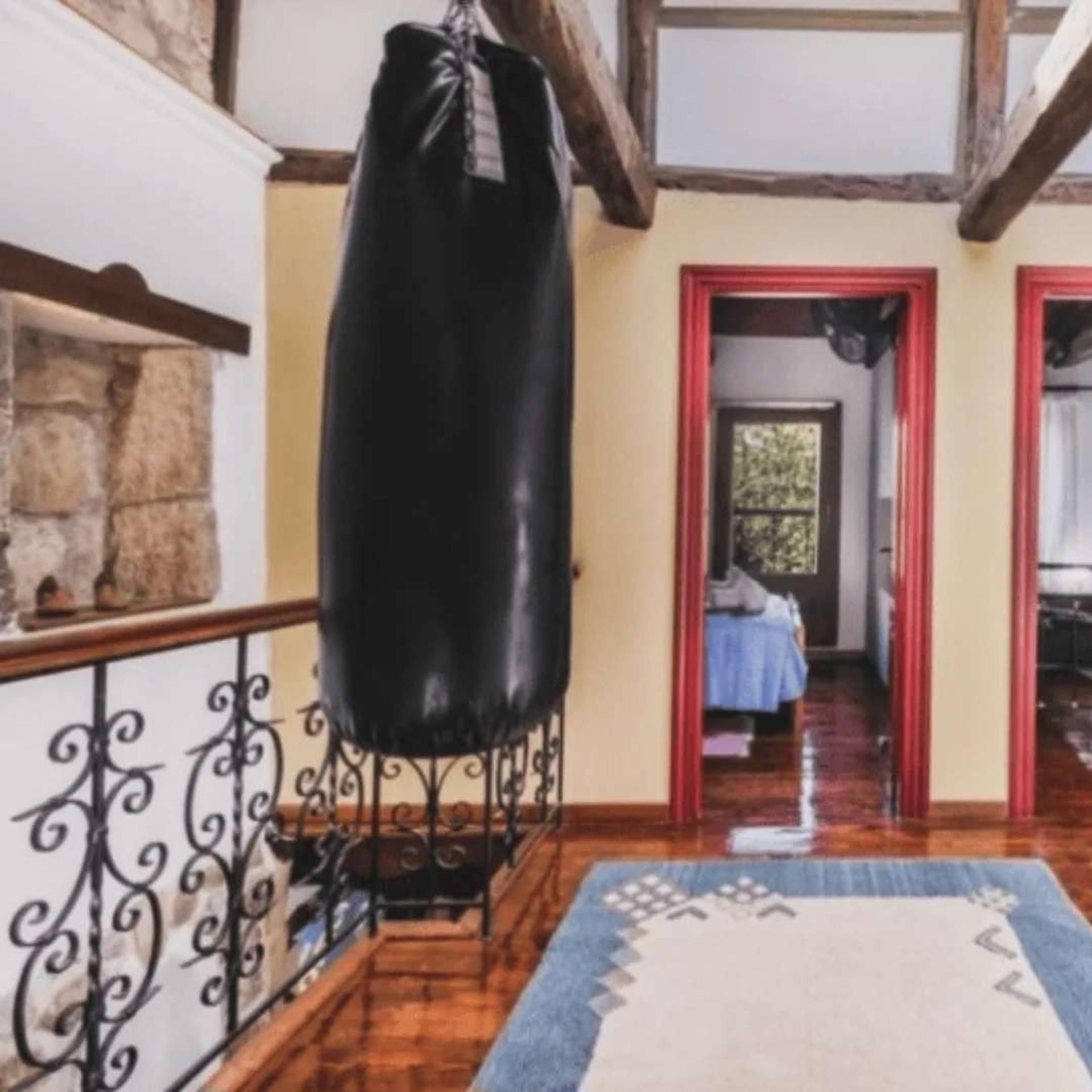 A room with a wooden floor, a black punching bag, a patterned rug, and a stone wall.