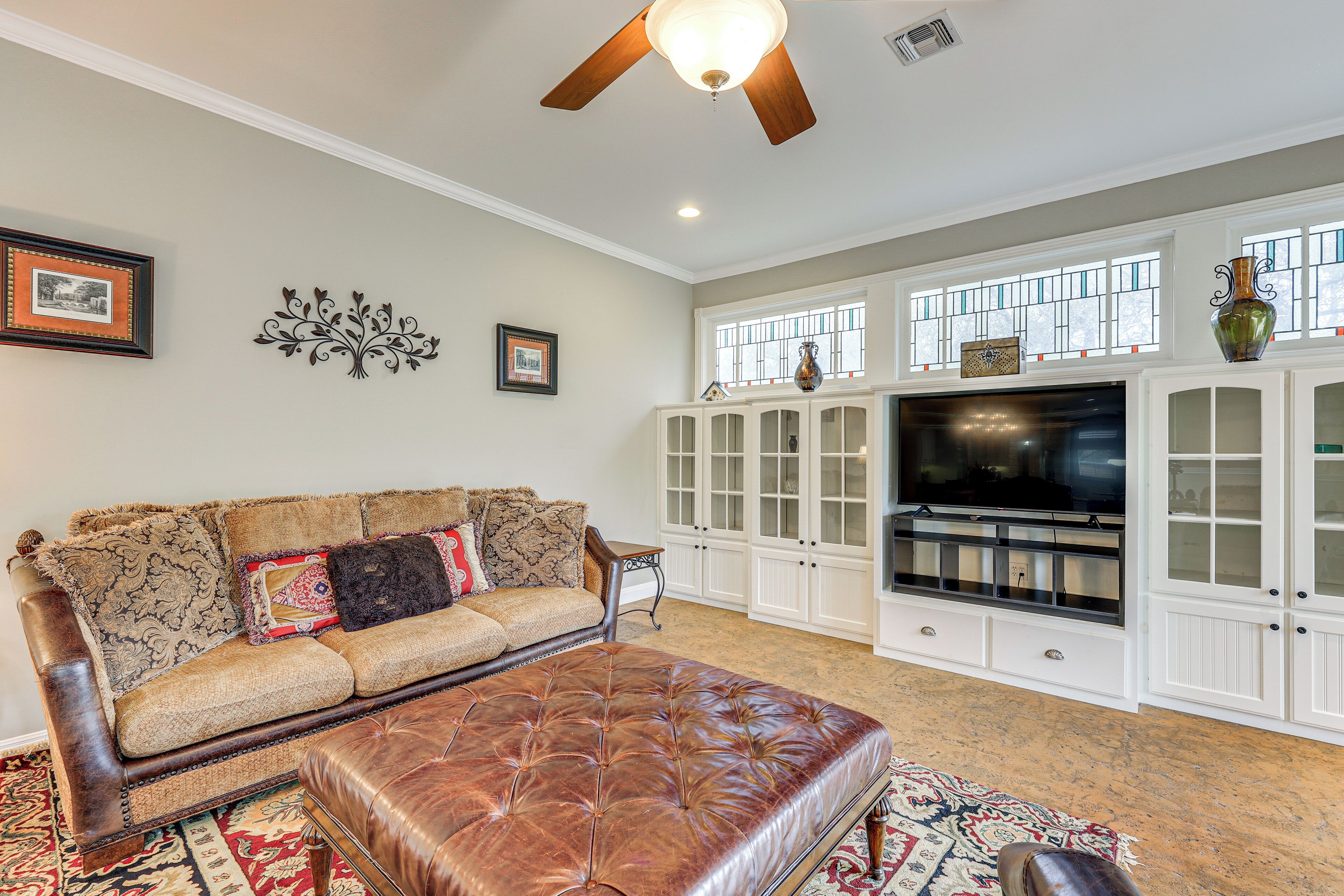 A living room with a brown leather sofa, a matching ottoman, a large flat-screen TV, and a decorative cabinet with glass doors.