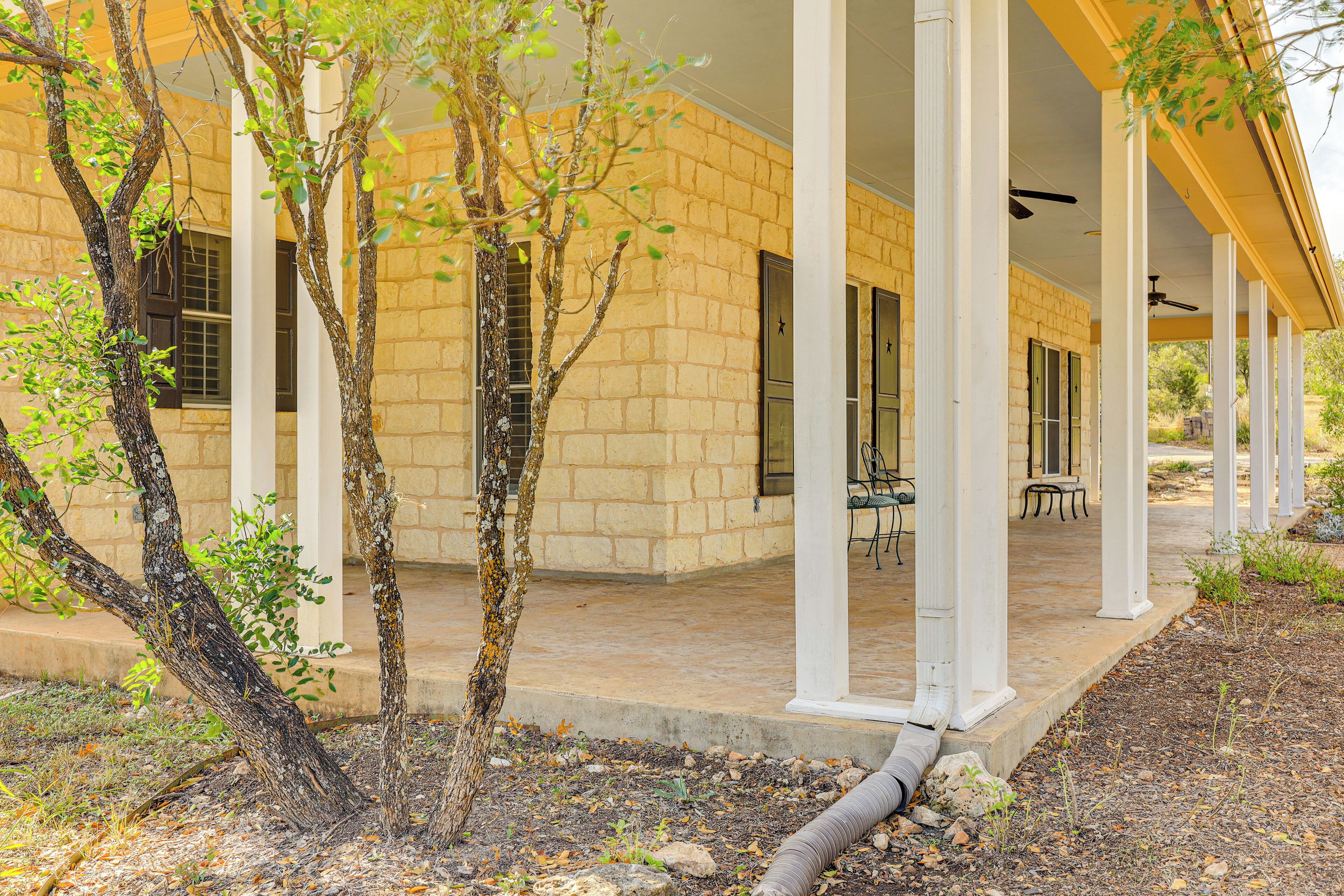 A covered outdoor area with brick walls, white columns, and a patio with tables and chairs.