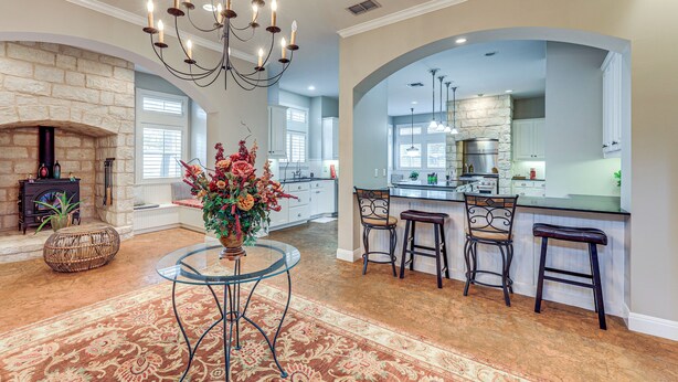 A spacious living room with a fireplace, a glass coffee table, and a chandelier. There is a kitchen area with a bar and stools. - Near Golfing & Parks: Serene San Antonio Home (San Antonio)