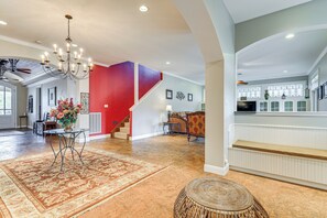 A spacious living area with a large chandelier, a red accent wall, and a staircase leading to an upper level.