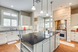 A modern kitchen with white cabinetry, a large island, a stone accent wall, and a stainless steel range hood. - Near Golfing & Parks: Serene San Antonio Home (San Antonio)