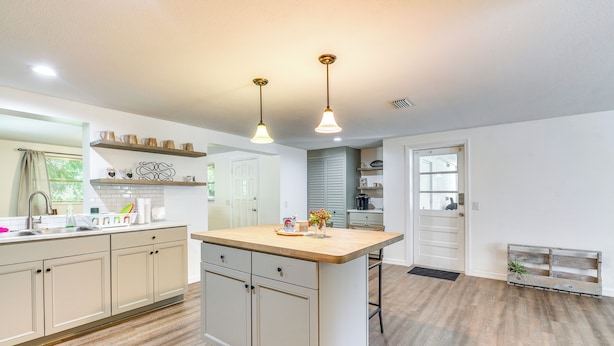 Een moderne keuken met een centraal eiland, hangende lampen en een houten bankje.