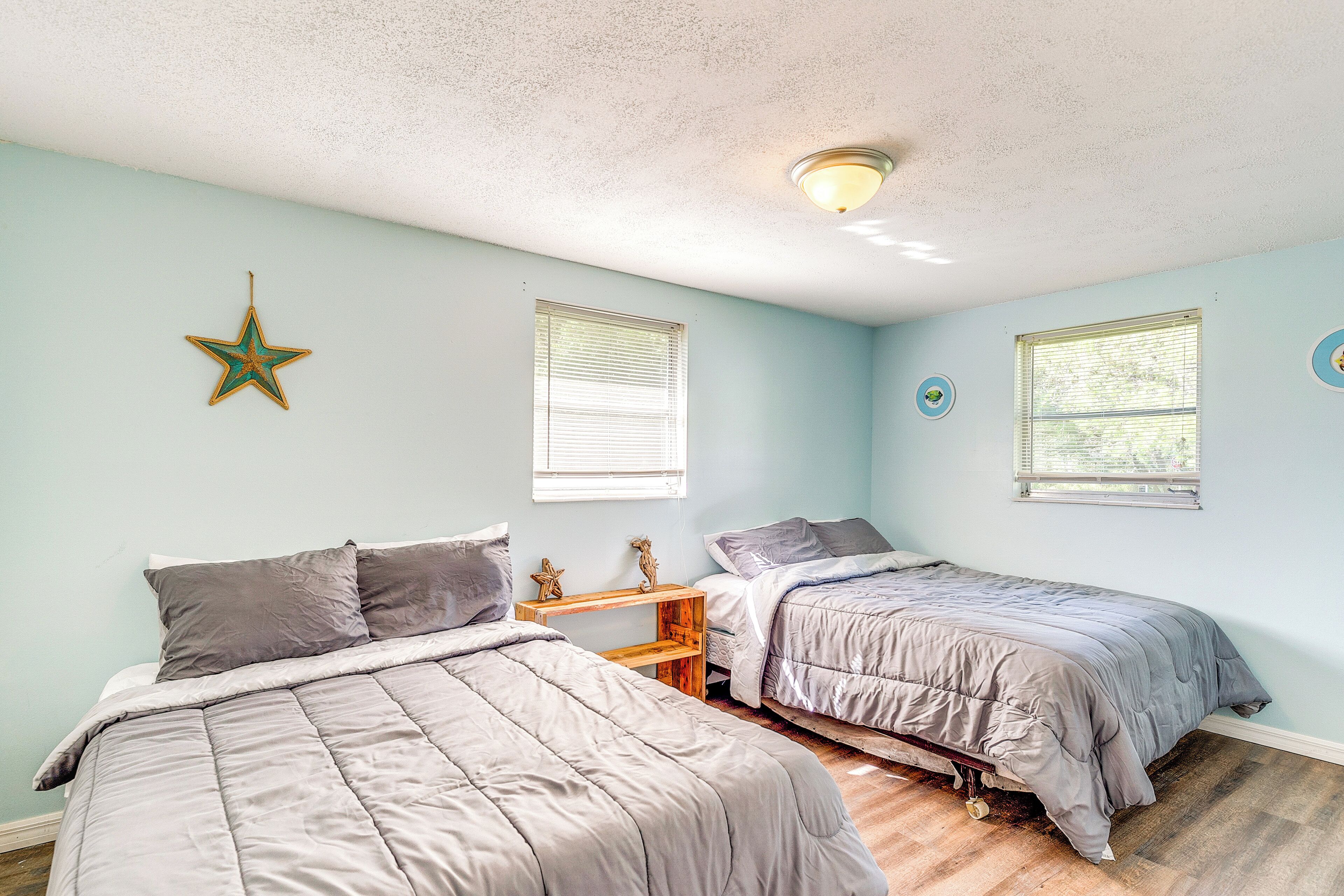 A bedroom with two beds, a star decoration, and two windows with blinds.