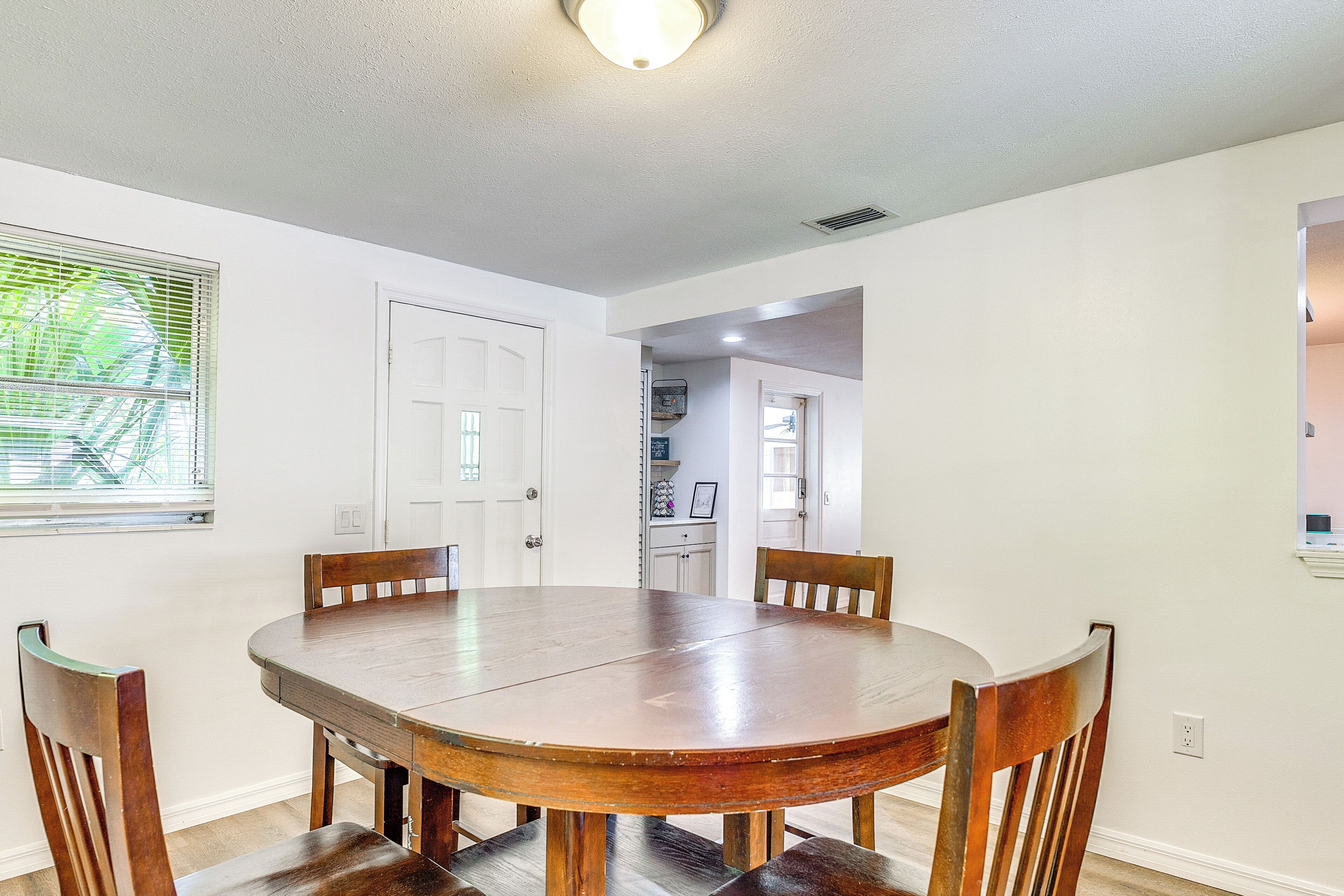 Comedor con una mesa redonda de madera y cuatro sillas, paredes blancas y una ventana con persianas.
