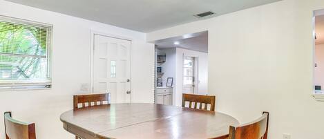 Comedor con una mesa redonda de madera y cuatro sillas, paredes blancas y una ventana con persianas.