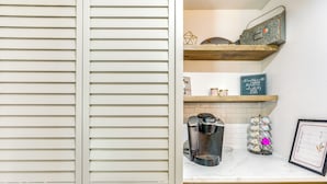 Een keuken met witte kastjes, een koffiezetapparaat, een decoratieve metalen dienblad en een menukaart in een lijst op het aanrecht.