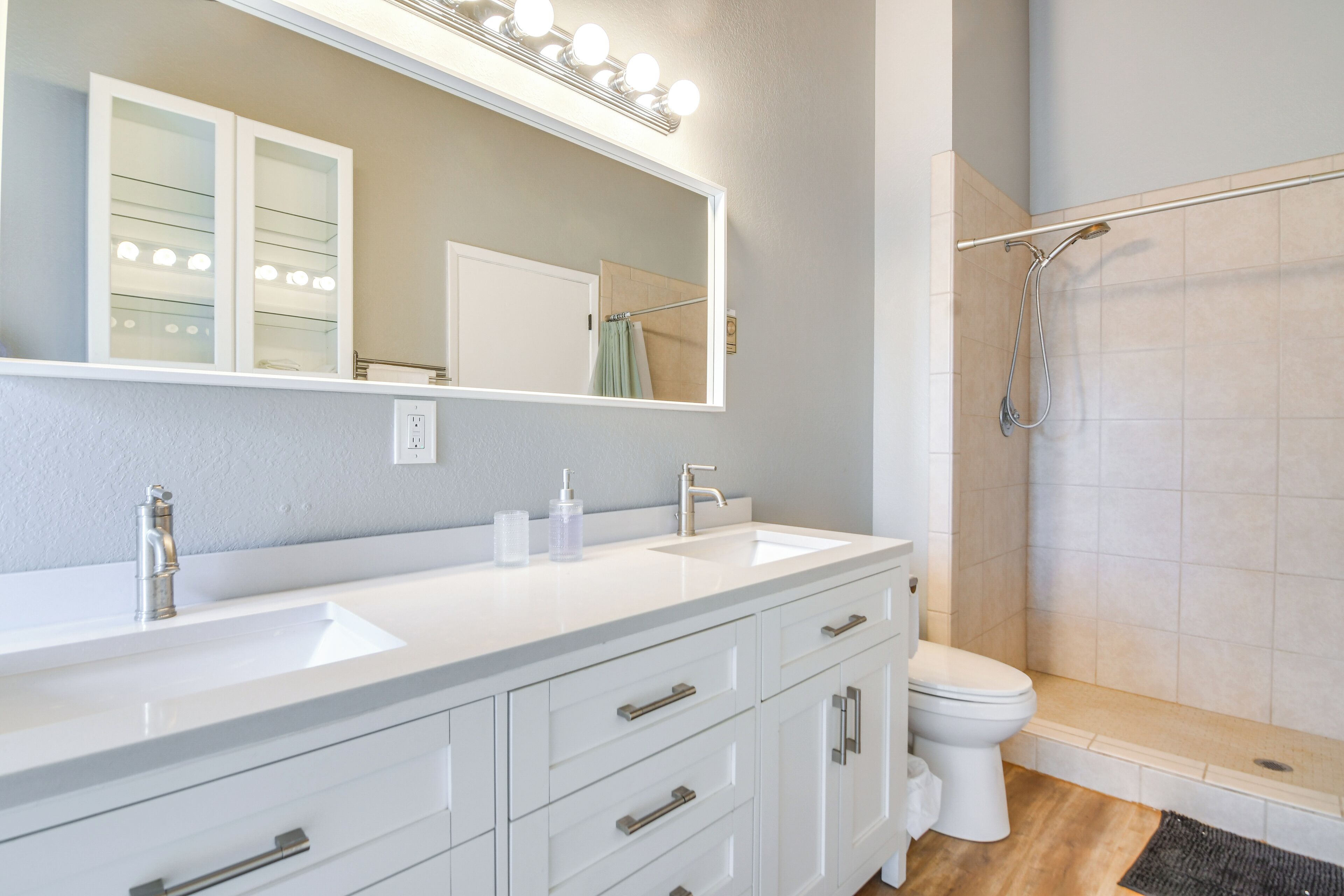 A bathroom with a white vanity, a large mirror with lights, a shower, and a toilet.