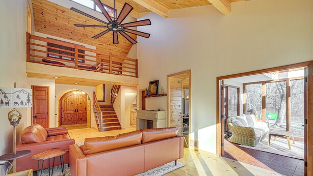 A spacious living area with a high ceiling, a wooden staircase, a leather sofa, and a dining area with a wicker chair. - Ski, Hike & More: Spacious Log Cabin in Long Pond (Pocono Summit)