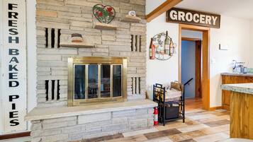 A kitchen with a stone fireplace, a 'Fresh Baked Pies' sign, and a 'Grocery' sign above the door.