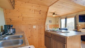 Una cocina con paredes de madera, estufa a gas, pileta y ventilador de techo.