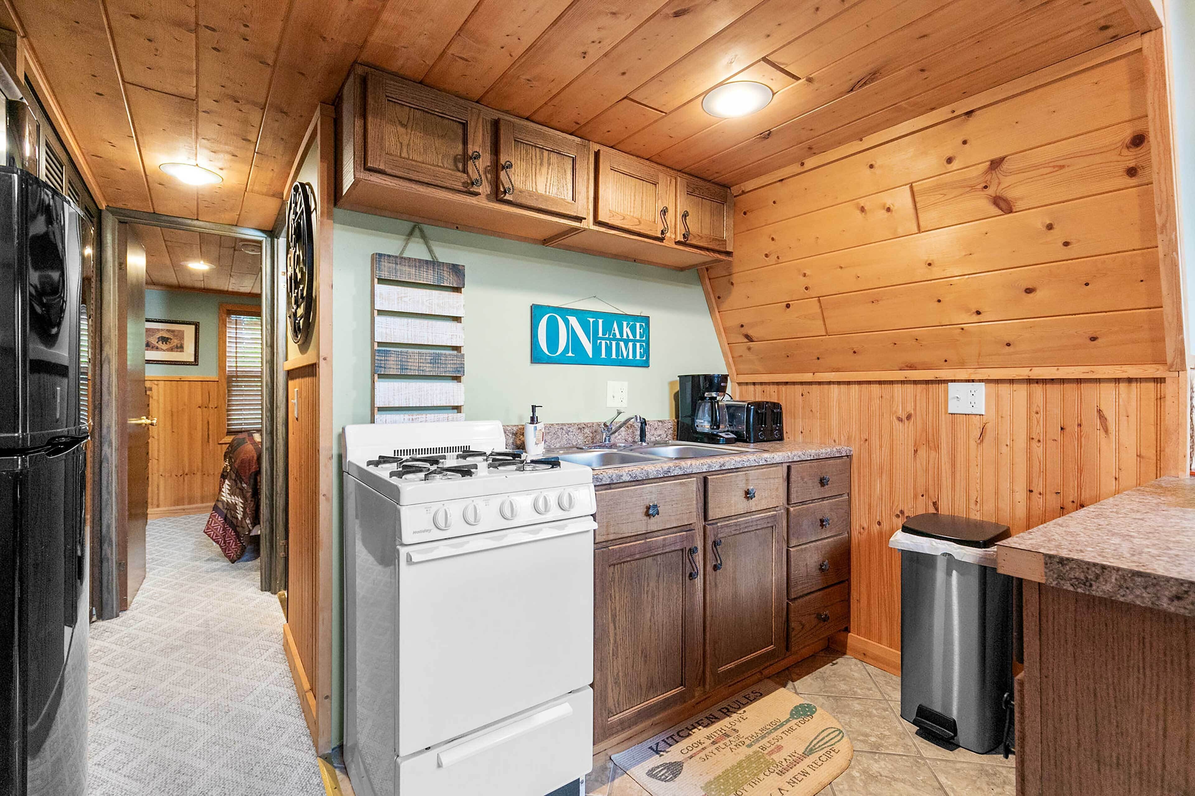 Una cocina con gabinetes de madera, estufa, fregadero y cubo de basura.