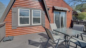 Una cabaña de madera con techo triangular, ventanas grandes y una terraza con mobiliario exterior.