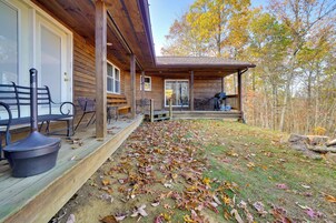 Una cabaña de madera con porche cubierto, mobiliario exterior y vistas al bosque circundante.