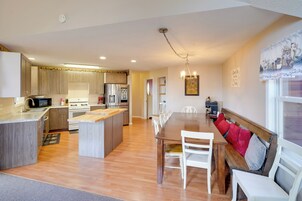 Una cocina moderna con armarios de madera, una isla central y un comedor con mesa de madera y sillas blancas.