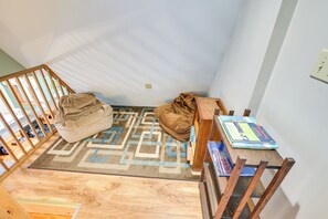 Ein Eckzimmer mit einem hölzernen Babybett, einem kleinen Tisch mit Büchern und einem gemusterten Teppich.