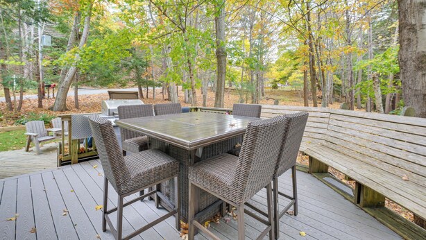 Een terras met een tafel met glazen blad en rieten stoelen, omringd door bomen en een houten bank.